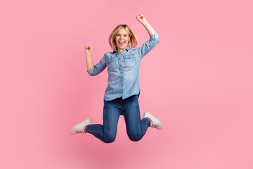Portrait of cheerful positive girl jumping in the air with raised fists looking at camera isolated on pastel background