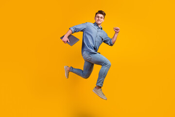 Photo of cheerful caucasian smart young man holding laptop smiling jumping high running isolated...