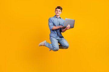 Fototapeta na wymiar Photo of cheerful caucasian young man holding laptop smiling jumping high running on isolated shine background