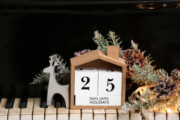 Calendar with text 25 DAYS UNTIL HOLIDAYS and Christmas decor on piano keys, closeup