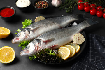 Fresh raw sea bass fish and ingredients on black table