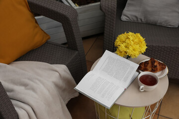 Different pillows, blanket, book and beautiful chrysanthemum flowers on garden furniture outdoors