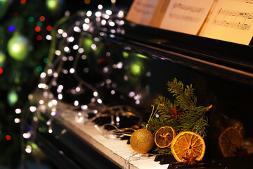 Fir branch with Christmas ball, orange slices and glowing lights on black piano, closeup