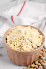 Chickpea flour in bowl and seeds on white marble table, closeup