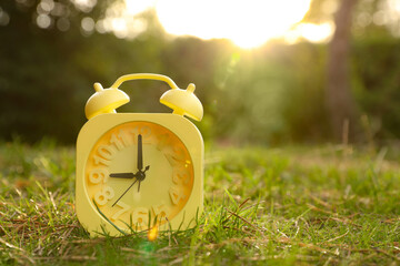 Yellow alarm clock on green grass outdoors. Space for text