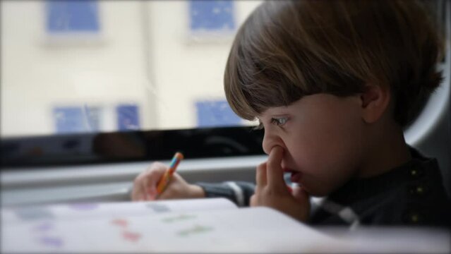 Concentrated Child nose picking while doing homework seated inside on a moving train
