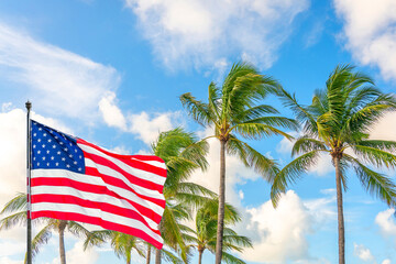 American flag waving against palm trees on blue sky background