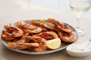 Plate of delicious cooked shrimps served with lemon, sauce and wine at table, closeup