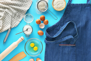 Denim apron, different ingredients and kitchen tools on light blue background, flat lay