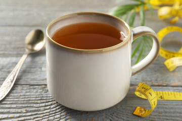 Cup of herbal diet tea and measuring tape on grey wooden table, closeup. Weight loss concept