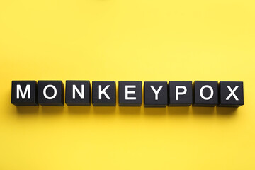 Word Monkeypox made of black wooden cubes on yellow background, top view