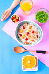 Porridge with milk, dried cherry and raisin in ceramic bowl and fresh orange juice on colorful background. Breakfast meal. Top view