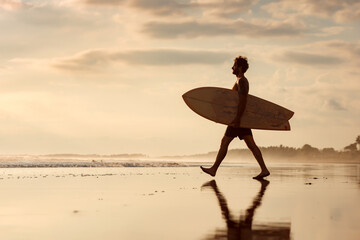 Handsome surfer walks at sunset sea beach - Powered by Adobe