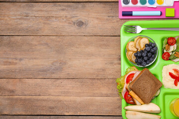 Flat lay composition with serving tray of tasty healthy food and school stationery on wooden table....