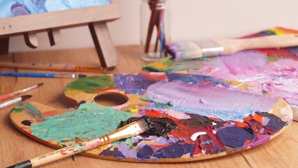 Obraz premium Artist's palette with mixed bright paints and brush on wooden table