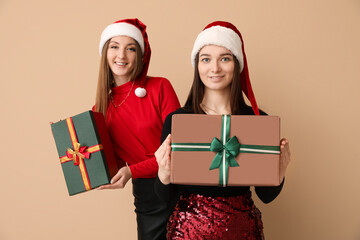 Young women in Santa hats with Christmas gifts on beige background