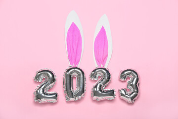 Figure 2023 made of balloons with paper bunny ears on pink background