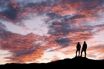 A silhouette of young adventurous couple watching the colourful sunset. High quality photo