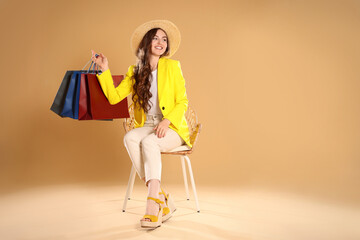 Happy woman holding many colorful shopping bags on armchair against beige background