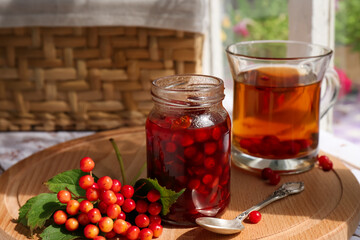 Tasty hot drink, jam and viburnum berries on wooden board indoors