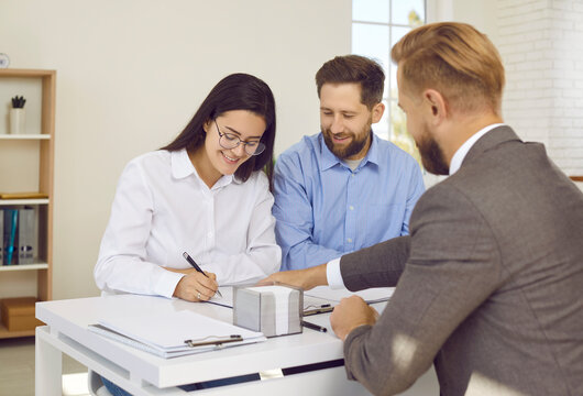 Young family buying apartment and signing contract at real estate agent's office. Happy couple sitting at table and putting their signatures on contract agreement. Mortgage, buying property concept