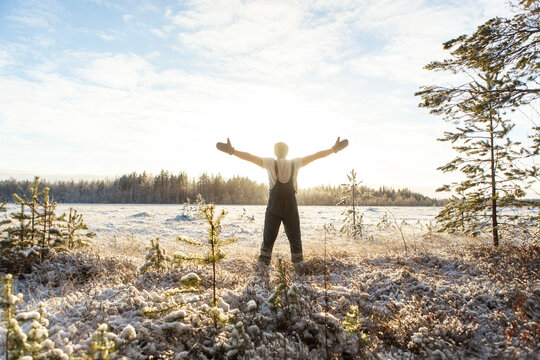 An athletic man raising his hands up with clean snow in the woods. Brutal man hardens to increase immunity. Nature power antistress winter concept