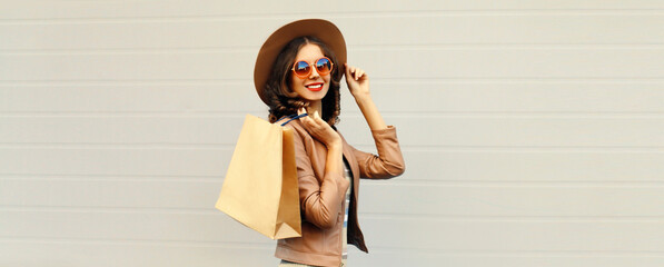 Portrait of beautiful happy smiling woman with shopping bags wearing jacket, round hat on gray background, blank copy space for advertising text