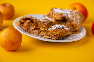 2 piece of apple strudel on white plate, 4 apple on yellow background, closeup.