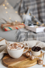 Still life with a mug of hot cocoa with marshmallows on the table among packing materials and Christmas decor.