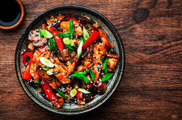 Stir fry chicken with paprika, mushrooms and chives in bowl. Asian cuisine dish. Wooden kitchen table background, top view