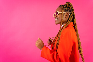 African young woman with braids on a pink background, portrait in the studio in a red outfit having fun