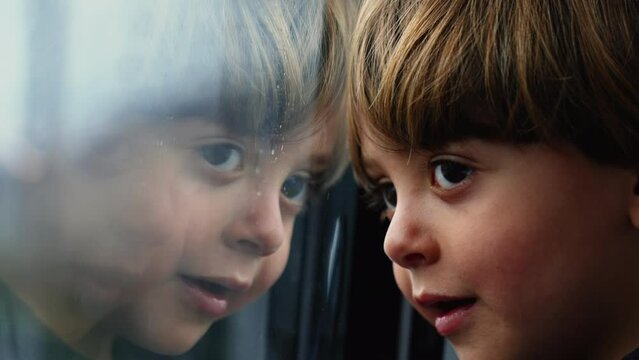 One pensive child leaning on train window. Mirror glass reflection of little boy traveling in high speed railroad train. Thoughtful kid watching landscape passing by
