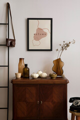 Creative composition of vintage living room interior with mock up poster frame, stylish sideboard, glass vase with dried flowers, black phone, pumpkins and personal accessories. Home decor. Template.