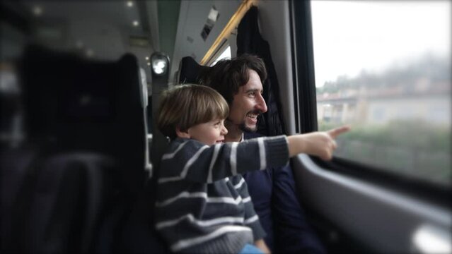 Happy father and son traveling together by train during vacation holidays. Little boy pointing with hand at landscape passing by inside transportation in motion