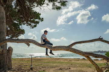 teenager climbing a tree against the blue sky in front of the sea,