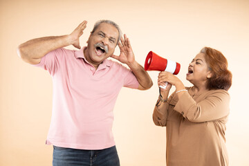 Senior indian woman scream or shouting at man in megaphone isolated on beige background. announce...