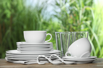 Set of clean dishware and glasses on wooden table against blurred background, space for text