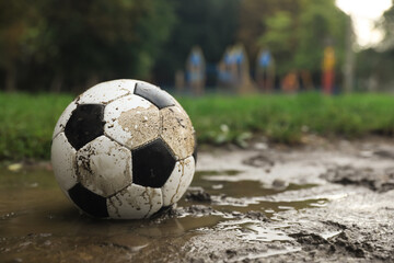 Fototapeta na wymiar Dirty leather soccer ball in puddle outdoors, space for text