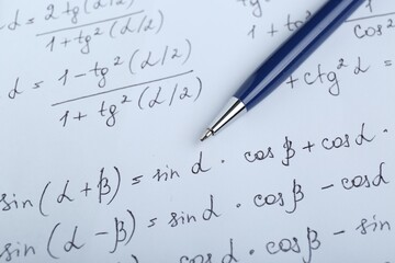 Sheet of paper with different mathematical formulas and pen, closeup