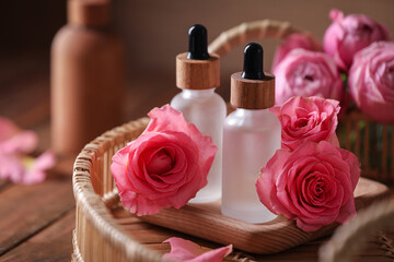 Obraz na płótnie Canvas Tray with bottles of essential rose oil and flowers on wooden table, closeup