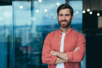 Portrait of a happy and smiling programmer in the middle of a modern office, a man in glasses and a...