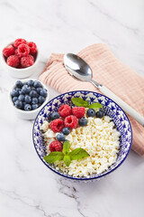 Cottage cheese in bowl decorated with raspberries and blueberries and mint leaves on white