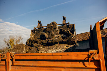 An excavator filling up truck with soil.