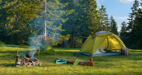 Tent and bonfire on the forest lawn in the mountains