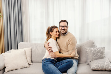 A happy couple is sitting in a living room at home and hugging.