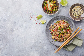 Wok with turkey meat, soba noodles, corn, green peas, green beans and carrots served on gray background with chopsticks. Asian food, concept of street food