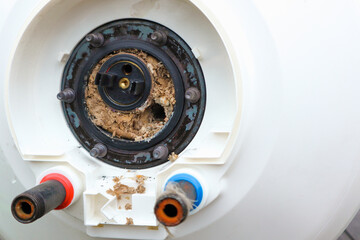 Water heater repair. Repair and maintenance of boilers. The master plumber pulls out a tubular electric heater covered with lime scale from the hole in the boiler.