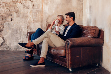 Obraz premium friends talking sitting on sofa - colleagues taking a break at work with a coffee