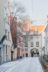 Beautiful narrow street with cobblestones in Riga Old Town with houses, buildings and restaurants in winter covered by the snow, vertical 