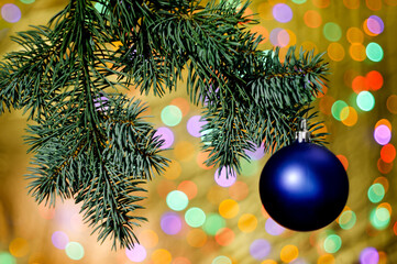 blue decorative christmas bubble hanging on a decorative twig chain with colorful lighting with bokeh in the background, space for text